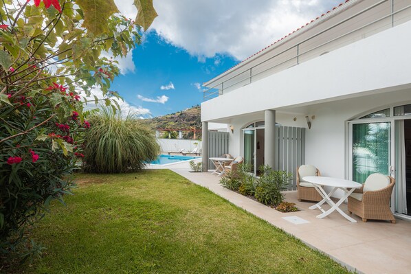 Ett modernt hus med pool, utomhusmöbler och frodig grönska.
