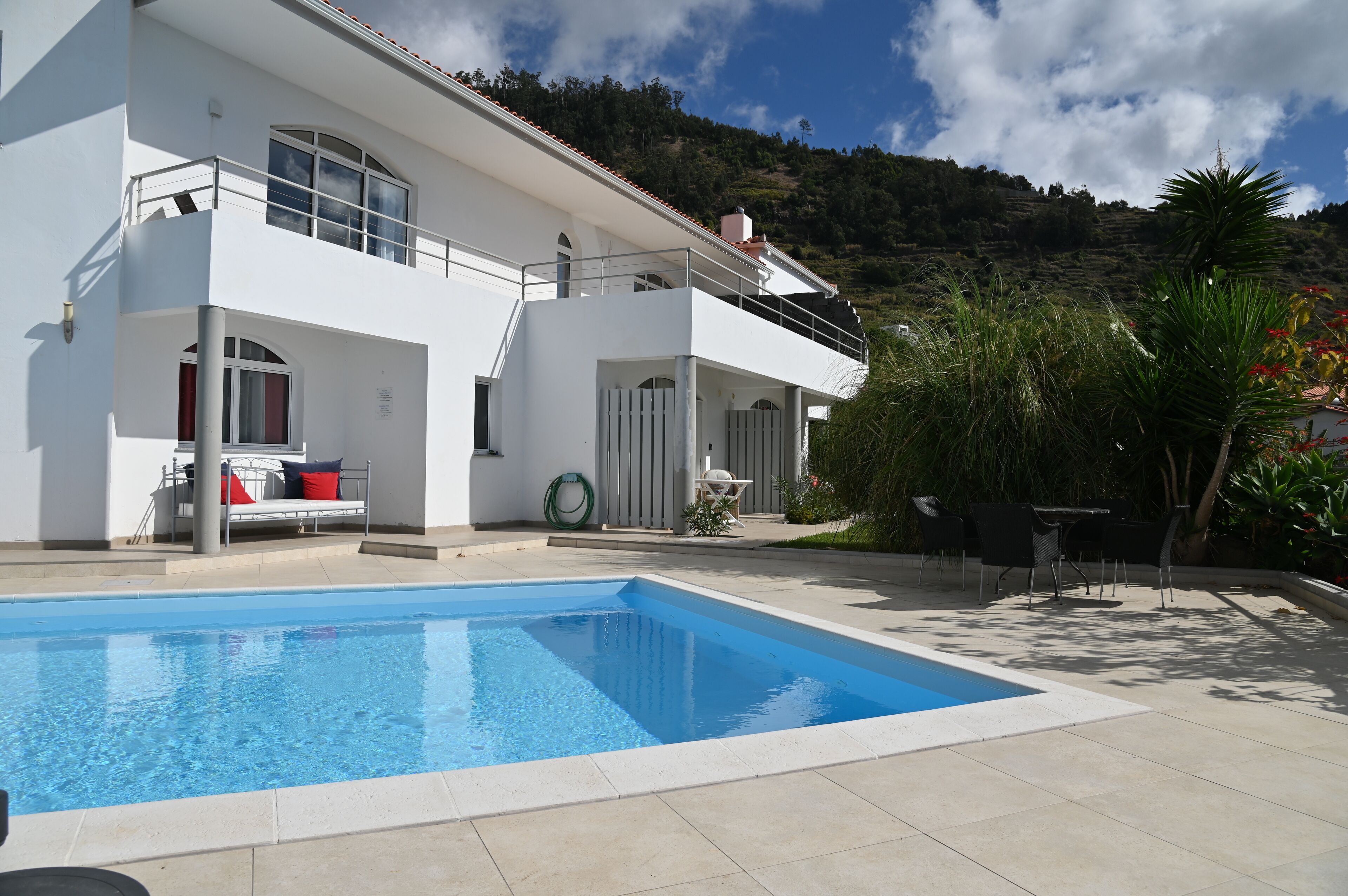 A modern two-story house with a swimming pool, outdoor furniture, and a view of a mountainous landscape.