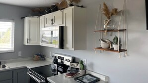 A modern kitchen with white cabinets, a built-in microwave, and a hanging plant shelf. - The Honeymoon Hideaway (Trenton)