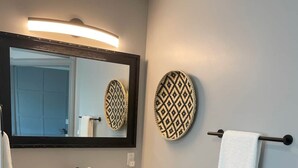 A bathroom with a dark marble vanity, a large mirror, a towel rack, and a patterned wall decoration. - The Honeymoon Hideaway (Trenton)