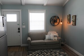 A compact living space with a kitchenette, a sofa, a patterned rug, and a wall-mounted clock. - The Modern Farm House (Trenton)