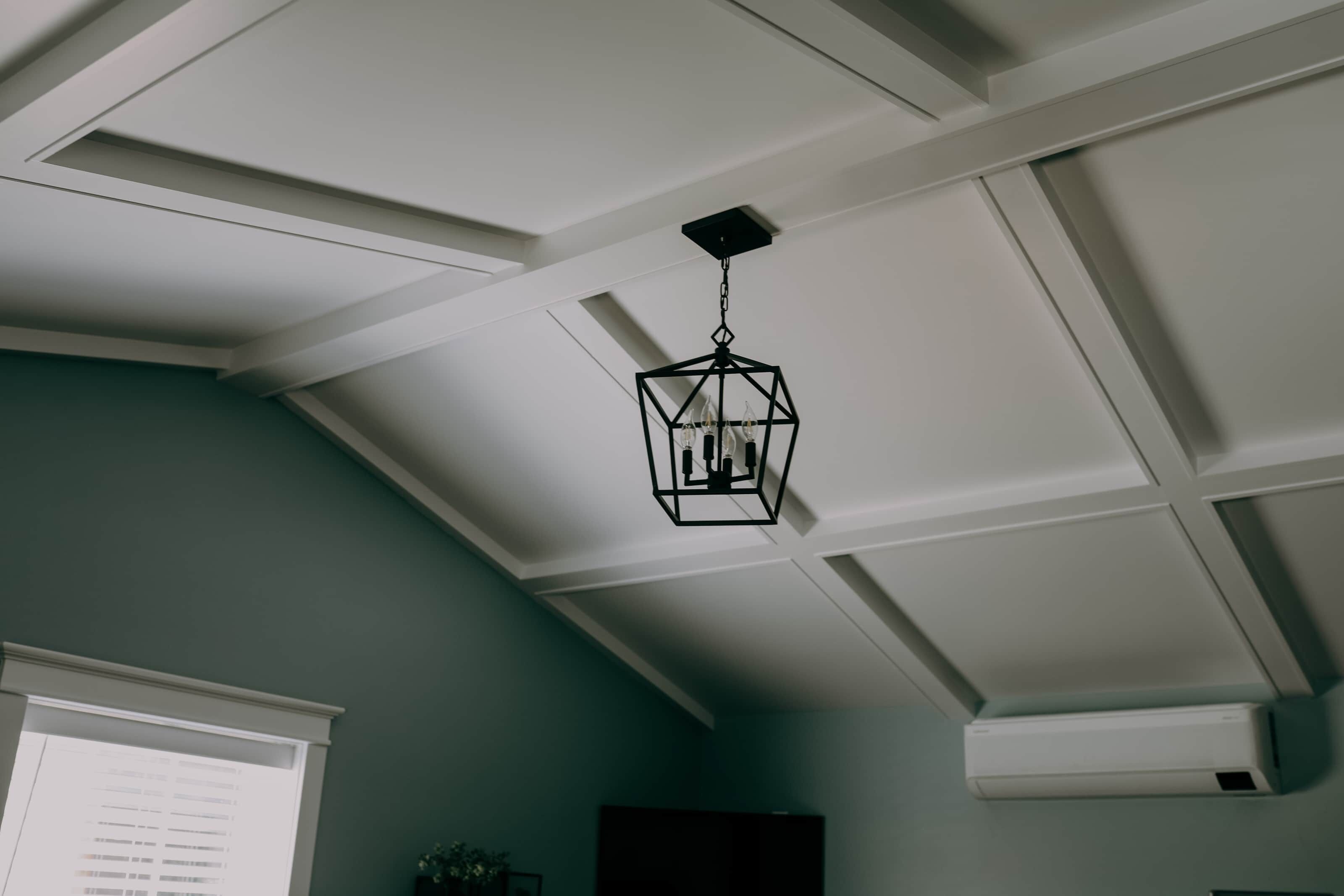 A room with a sloped ceiling, a hanging geometric light fixture, and a white air conditioning unit.