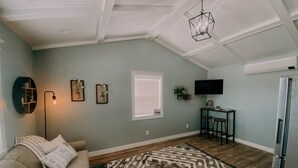 A living room with a sofa, a patterned rug, a ceiling light, wall art, a TV, and a refrigerator. - The Modern Farm House (Trenton)
