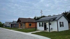 A row of single-story cabins with attached porches, a gravel driveway, and a grassy lawn. - The Modern Farm House (Trenton)