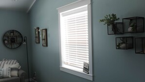 A room with a large window, a sofa, and wall-mounted decor including a clock and framed pictures. - The Modern Farm House (Trenton)