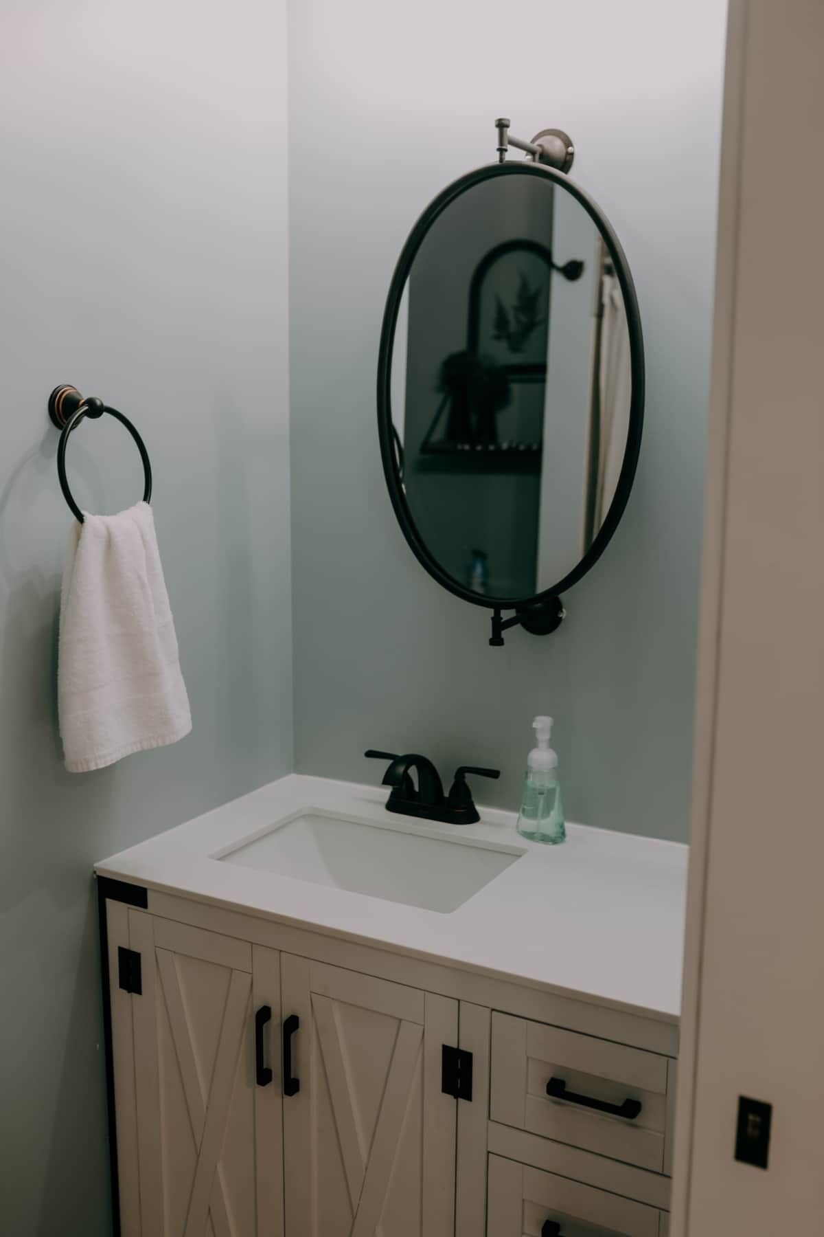 A bathroom with a white sink, a black faucet, a round mirror, and a towel hanging on a black ring.