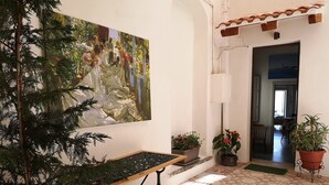 A hallway with a tiled floor, a painting on the wall, and potted plants. - The terraces (Sciacca)