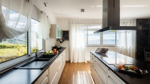 A modern kitchen with a large window, wooden flooring, and a view of a vineyard.