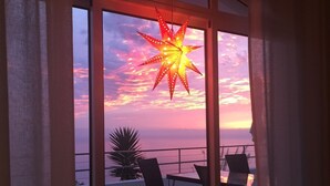 A balcony with chairs and a star-shaped light fixture, overlooking a sunset with a pink and purple sky.