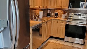 Een moderne keuken met roestvrijstalen apparatuur, houten kastjes en een betegelde vloer.