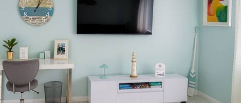 Un saló modern amb televisió de pantalla plana, un rellotge, una taula de treball, una cadira, una prestatgeria i objectes decoratius.