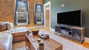 Een woonkamer met een bakstenen muur, een leren bank, een salontafel met een kom popcorn, een flatscreen televisie en een boekenkast.