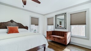 A bedroom with a large bed, a brown leather sofa, a ceiling fan, and a large mirror. - Kessler Park Retreat - Walking distance to Bishop Arts District  (Dallas)