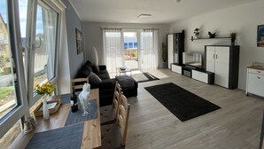 A modern living room with a sofa, a dining table with chairs, a TV, and a kitchen area.