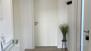 A hallway with a white door, a small plant, and a glass cabinet with a sign.