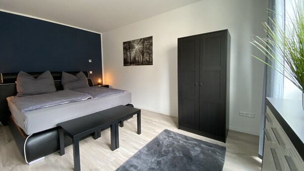 A modern bedroom with a bed, bench, wardrobe, and artwork.