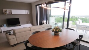 A modern living room with a round wooden dining table, beige sofa, and a TV on a white cabinet. - Luxury south facing 3 bedroom apartment in Las Colinas Golf (Dehesa de Campoamor)