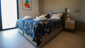 A neatly made bed with a floral bedspread, a bedside table with a lamp, and a wall with a colorful abstract painting. - Luxury south facing 3 bedroom apartment in Las Colinas Golf (Dehesa de Campoamor)