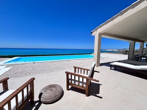 Un espace aménagé au bord de la piscine avec vue sur la mer, un coin salon couvert et un fauteuil de relaxation.