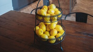 Una cucina con un tavolo in legno, un cesto a tre scomparti pieno di limoni e lampade dal design moderno.