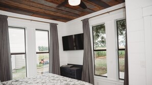 Una camera da letto con un letto, una TV a schermo piatto montata a parete e ampie finestre con tende.