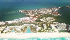 Vue aérienne d’une station balnéaire comprenant plusieurs bâtiments, une plage et un grand espace piscine.