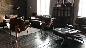 En moderne stue med en murstensvæg, lædersofaer, et træbord og en sort læderpuf.