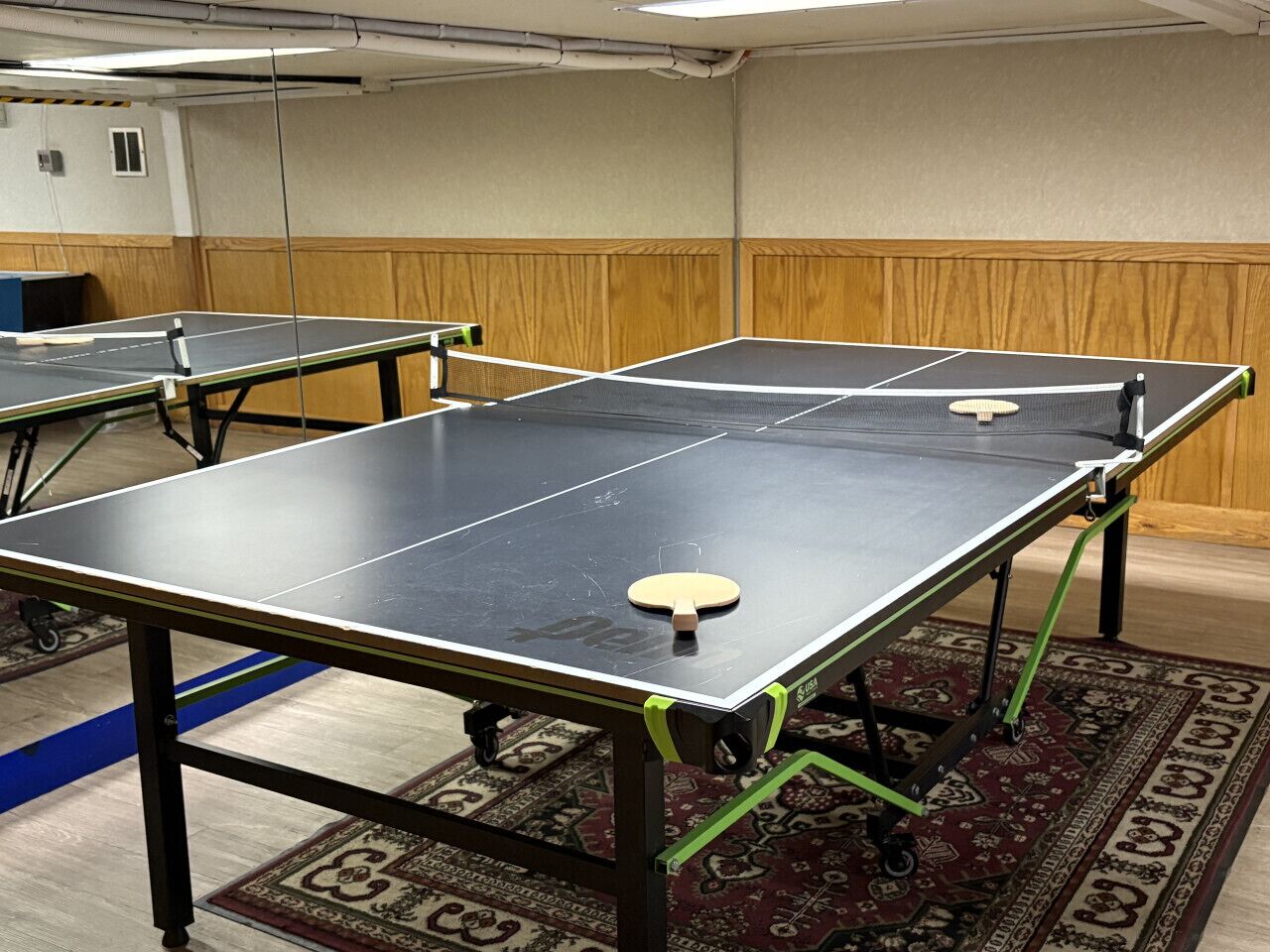 Una habitación con mesas de ping pong, alfombra estampada y paneles de madera.