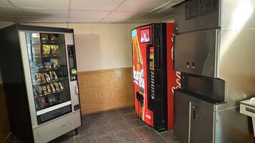 Un área con máquinas expendedoras, incluyendo una máquina de Coca-Cola, una máquina de aperitivos y un refrigerador de acero inoxidable.