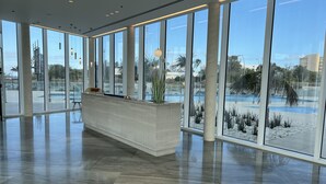 Un vestíbulo amplio con grandes ventanales, un mostrador de recepción y vistas a una zona de piscina.