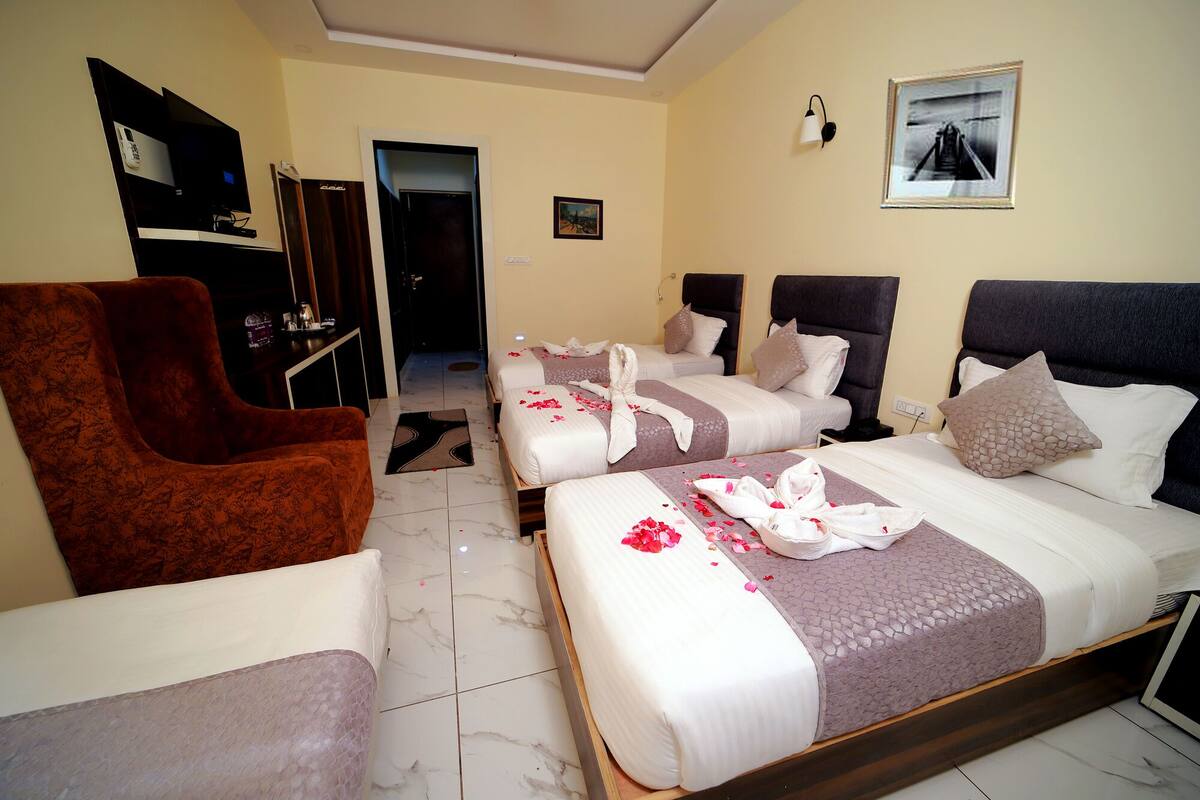 A hotel room with three beds, a brown armchair, a desk with a computer, and a framed picture on the wall.
