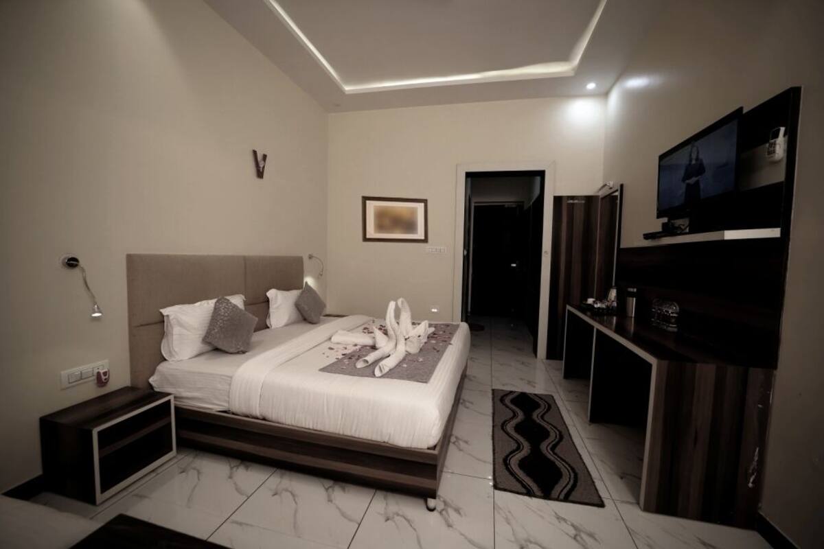A modern hotel room with a large bed, a flat-screen TV, a desk, and a walk-in closet.