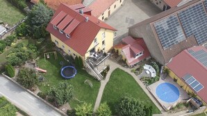An aerial view of a residential area with a yellow house featuring a red roof, a blue trampoline, and a swimming pool. - Beautiful spacious apartment (Gaukönigshofen)