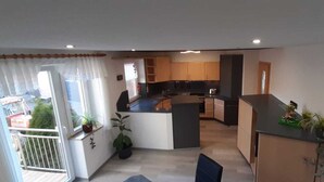 A modern kitchen with wooden cabinets, a central island, and a dining area with a chair. - Beautiful spacious apartment (Gaukönigshofen)
