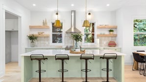 Uma cozinha moderna com uma ilha grande, luminárias pendentes e banquetas.