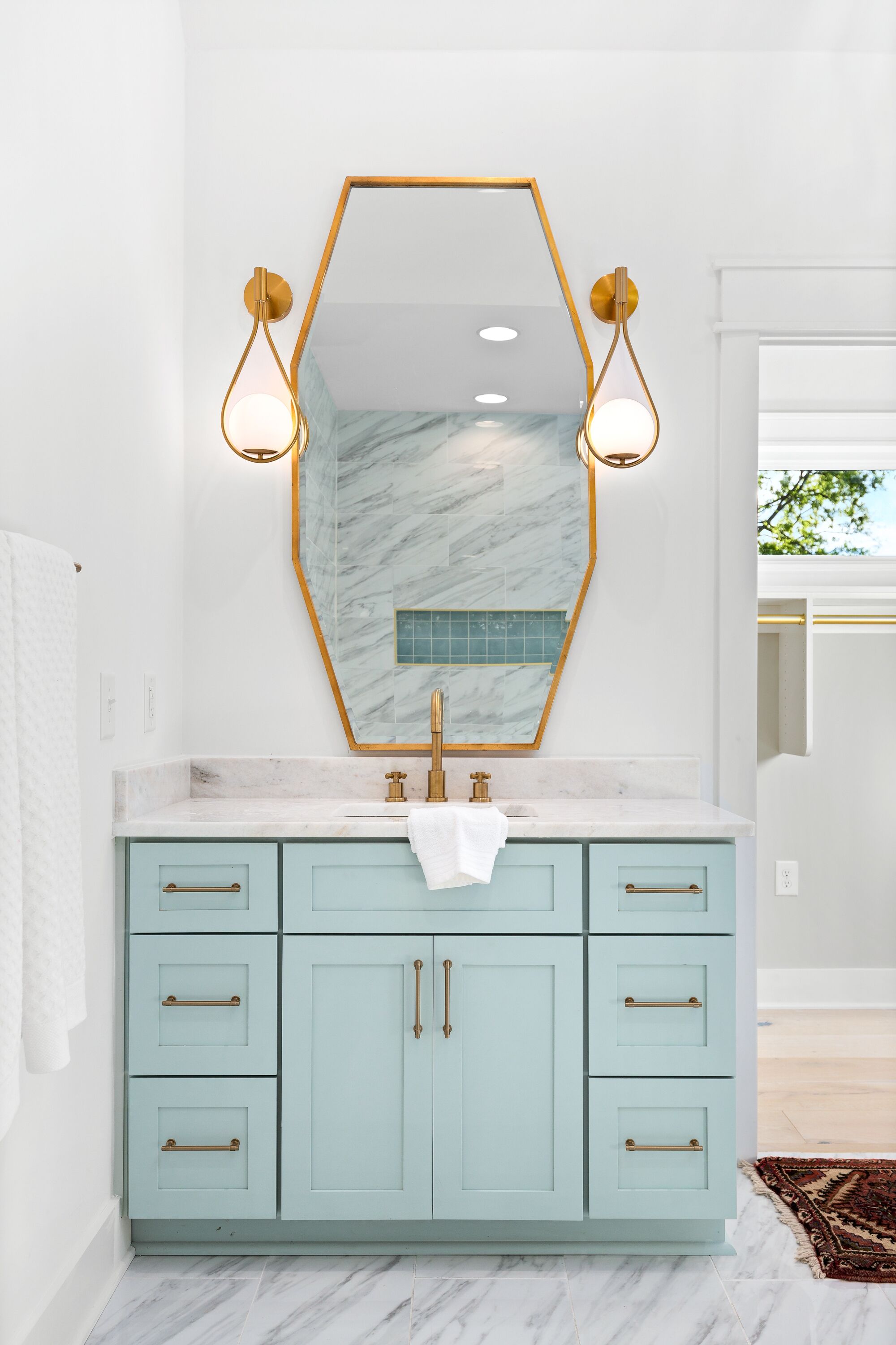 Une salle de bain avec un meuble-lavabo bleu clair, un grand miroir avec un cadre doré et deux appliques murales.