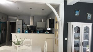 A modern kitchen with white cabinetry, a dining area with a white table and chairs, and a living area with a sofa. - In Casteljaloux at the door of the Landes pretty villa of 190m² - French property (Casteljaloux)