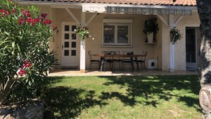 A house with a tiled roof, a covered patio with a table and chairs, and a garden with red flowers. - In Casteljaloux at the door of the Landes pretty villa of 190m² - French property (Casteljaloux)