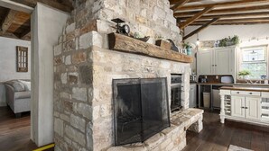 A stone fireplace with a screen, wooden beams, and a kitchen area with cabinets and appliances. - Authentic 1770's Home/PERFECT LOCATION/Steps to Marktplatz/Main! Hummingbird (Fredericksburg)