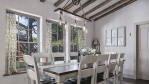 A dining area with a wooden table and white chairs, large windows with curtains, and hanging light fixtures. - Authentic 1770's Home/PERFECT LOCATION/Steps to Marktplatz/Main! Hummingbird (Fredericksburg)
