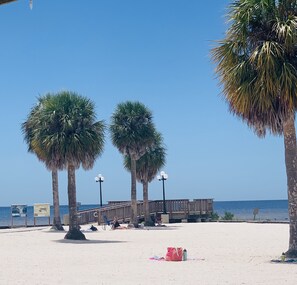 Ein Strand mit Palmen, einer Holzsteg und einem Rettungsschwimmerstand.