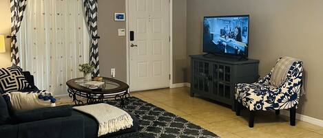 A living room with a sofa, a coffee table, a TV, a ceiling fan, and a patterned rug.