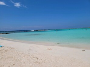 A beach with clear turquoise water, a sandy shore, and a few scattered rocks.