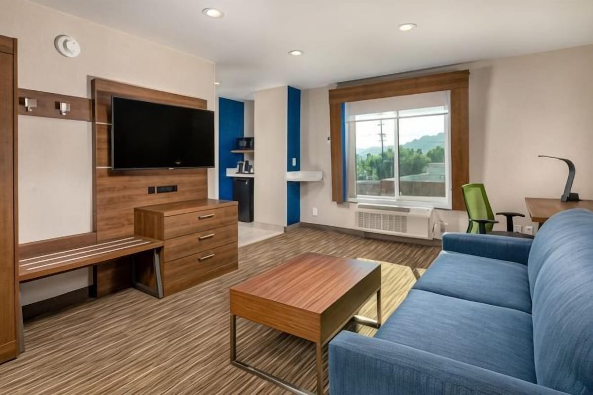A modern living room with a flat-screen TV, wooden furniture, a blue sofa, and a large window.