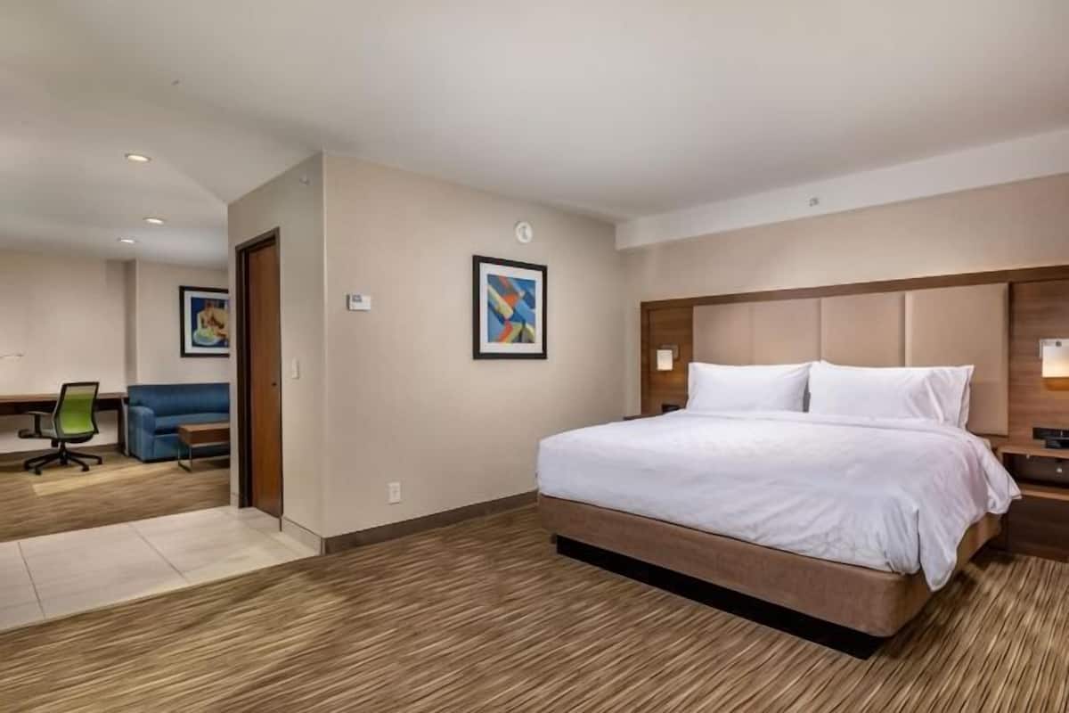 A hotel room with a large bed, a desk, a chair, and a painting on the wall.
