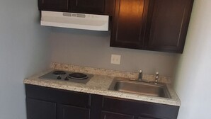A small kitchen with dark wooden cabinets, a granite countertop, a stainless steel sink, and a white trash bin. - Town & Country Motel (Fort Stockton)