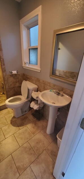 Een badkamer met toilet, wastafel en een raam boven het toilet.