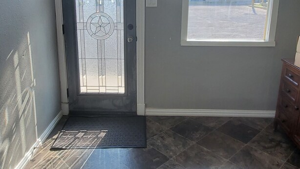 A room with a ceiling fan, a door with a decorative glass panel, a window with a view of the outside, and a tiled floor. - Town & Country Motel (Fort Stockton)