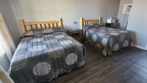 A bedroom with two wooden beds, a nightstand, a lamp, and a microwave. - Town & Country Motel (Fort Stockton)