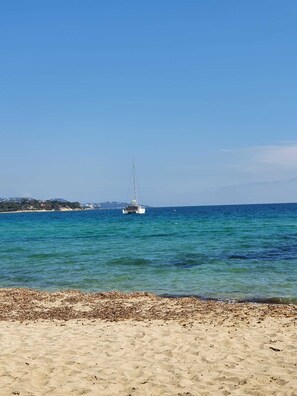 Ein Strand mit einem Segelboot im Wasser und einer fernen Küstenlinie mit Gebäuden.